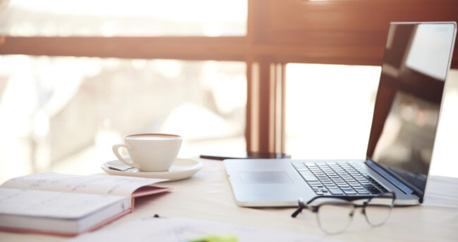 Lateral foreground of a working desk with the laptop, cup of cof