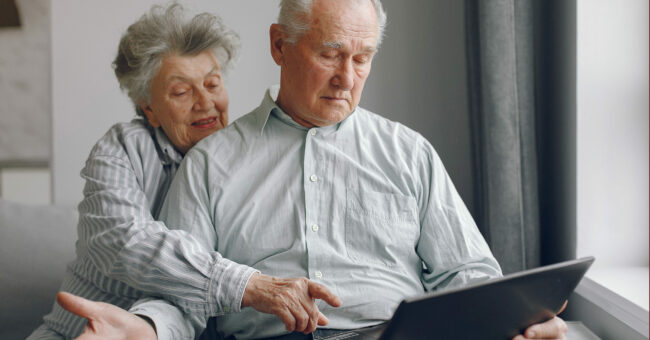 Elegant old couple sitting at home and using a laptop